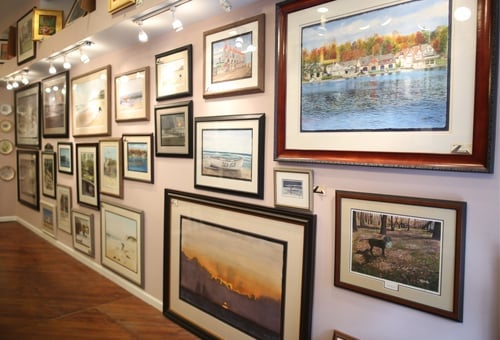 Gallery wall displaying framed landscape photographs and artwork on white and purple walls with wooden flooring