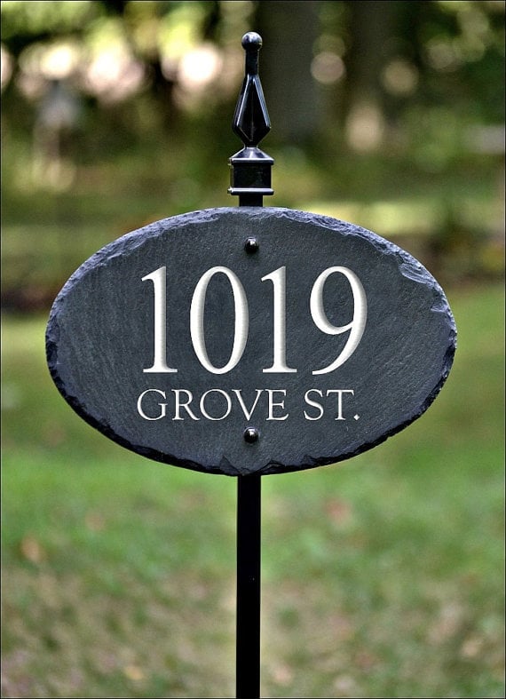 Black slate oval address sign reading 1019 Grove St. mounted on a pole in a garden setting