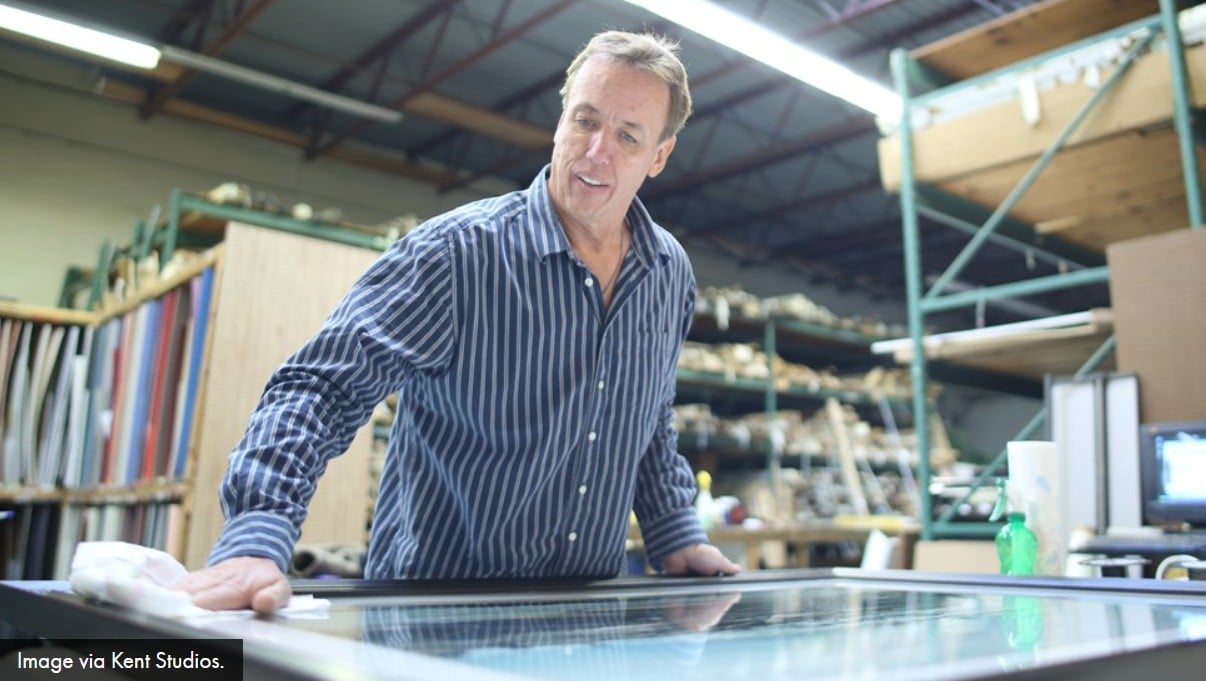 Middle-aged man in striped shirt leaning on desk in warehouse workspace with shelves and storage in background